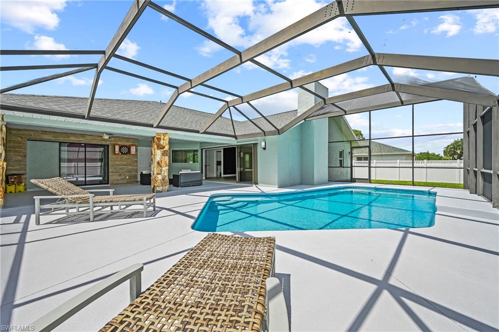 Screened-in outdoor living space with a free-form swimming pool, extensive concrete decking, and a covered patio area