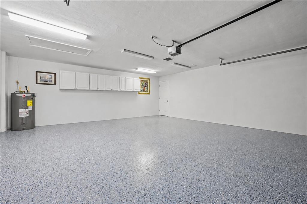 Spacious garage featuring a speckled epoxy floor, extensive overhead white cabinetry for storage, and bright overhead fluorescent lighting