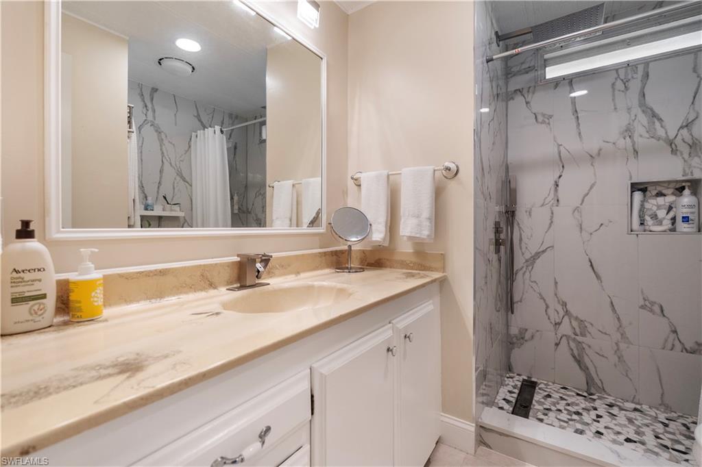 Walk-in shower featuring large-format marble-look wall tiles and a mosaic pebble floor