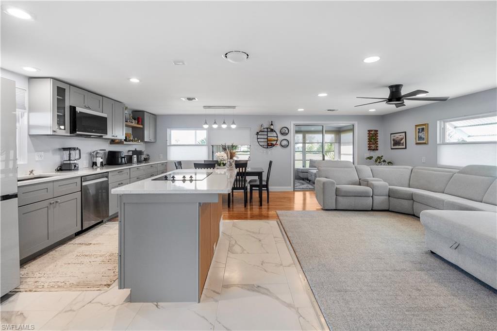 Open-concept living area featuring a kitchen with gray cabinetry, white countertops, and stainless steel appliances, a dining area with wood-finish flooring, and a living space with a ceiling fan