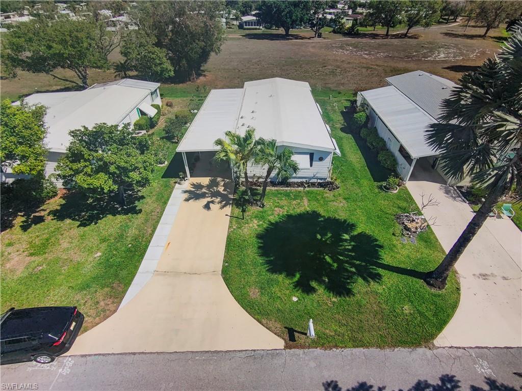 Property featuring a long driveway, attached carport, mature palm trees, and a spacious green lawn