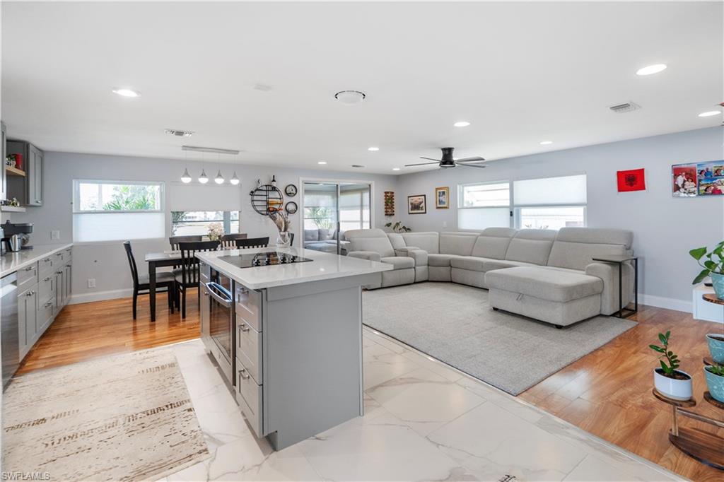 Open-concept living area featuring a kitchen island with cooktop, light wood-finish flooring, white marble-look tile, gray cabinetry, and recessed lighting
