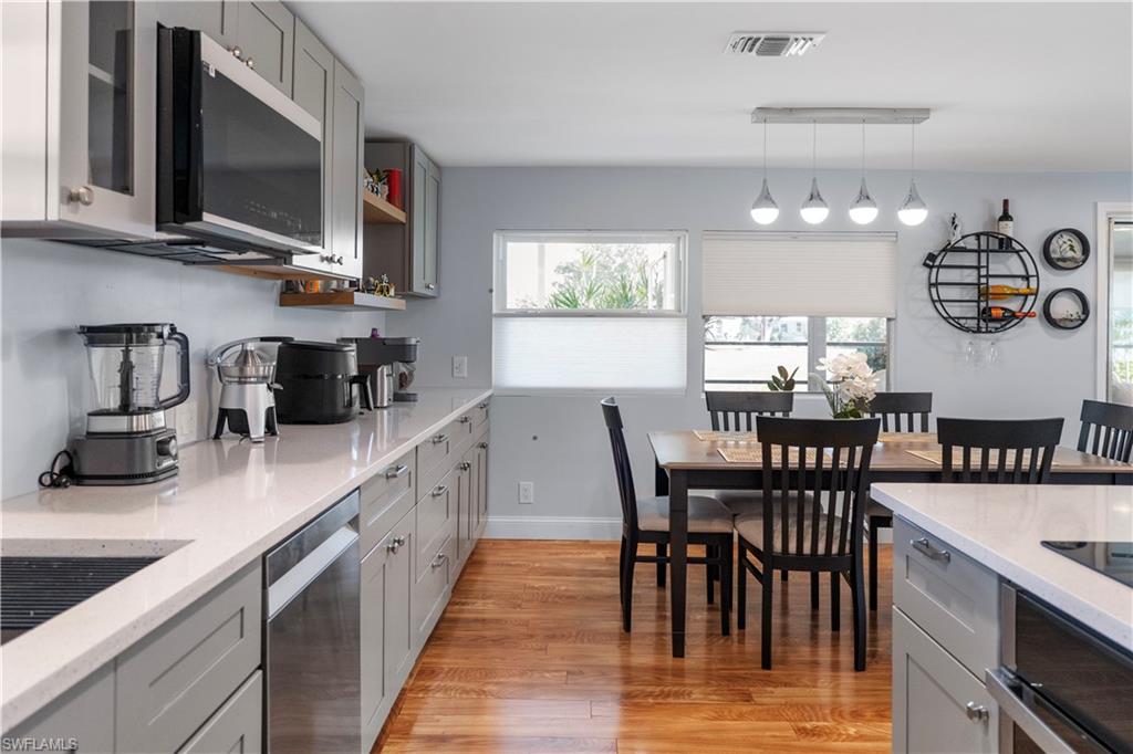 Modern kitchen featuring light gray cabinetry, light countertops, wood-finish flooring, stainless steel appliances, and a dining area with pendant lighting