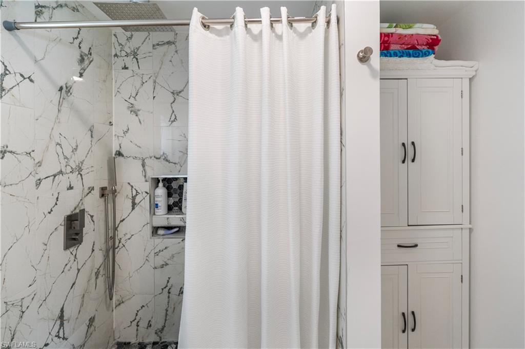 Shower enclosure featuring white and grey veined tile, brushed nickel fixtures, and a recessed niche with mosaic tile