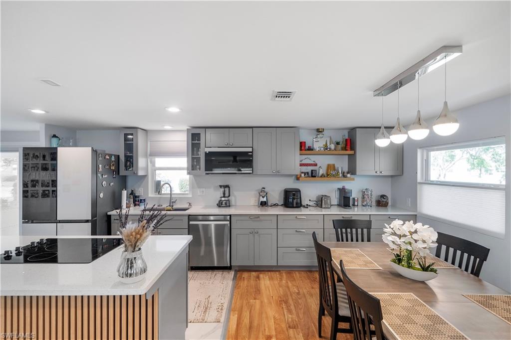 Open-concept kitchen featuring gray shaker-style cabinetry, stainless steel appliances, quartz countertops, and wood-finish flooring