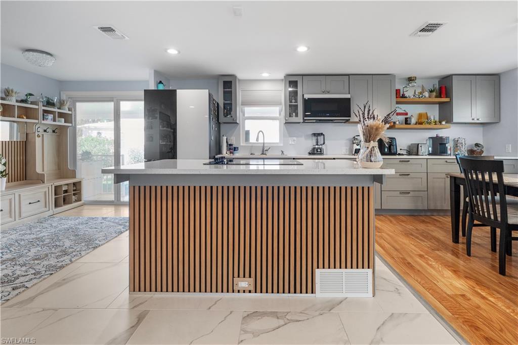 Contemporary kitchen featuring a wood-slat island with a light-toned countertop, gray cabinetry, built-in microwave, and wood-finish flooring