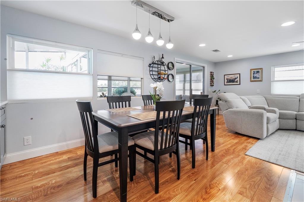 Open-concept living area featuring wood-finish flooring, recessed lighting, a modern linear pendant light fixture, and multiple windows with privacy blinds