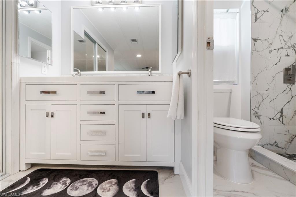 Dual vanity with white cabinetry and chrome hardware, featuring a large mirror and overhead lighting