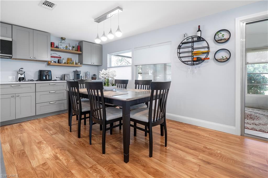 Kitchen and dining area featuring light gray cabinetry, white countertops, wood-finish flooring, and a modern linear pendant light fixture