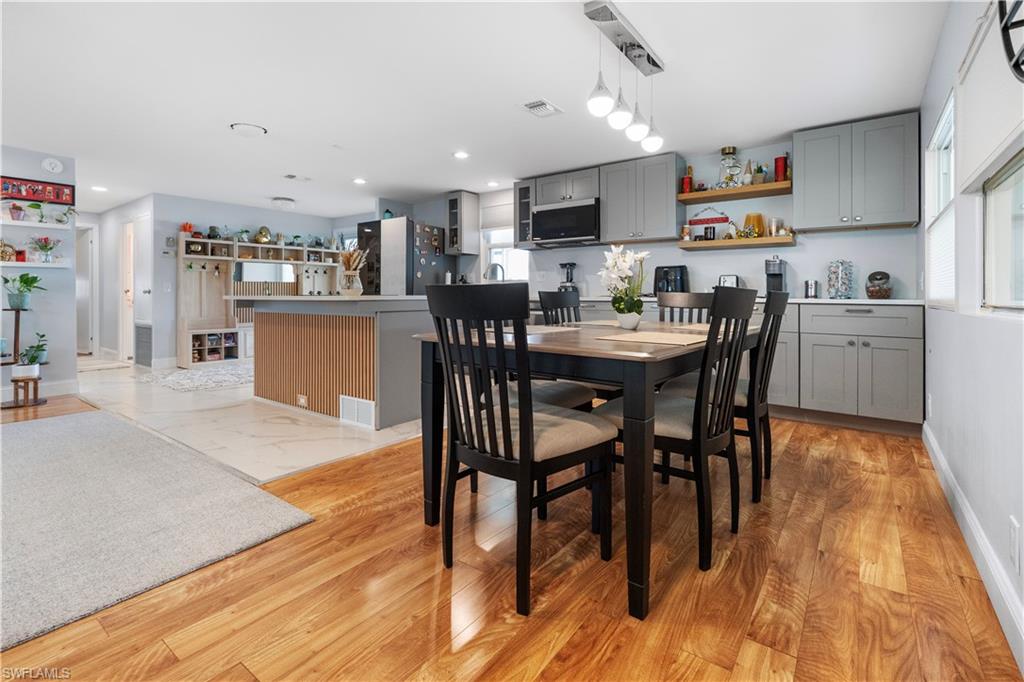 Open-concept kitchen and dining area featuring wood-finish flooring, grey cabinetry, white countertops, a central island, and a dining table with seating