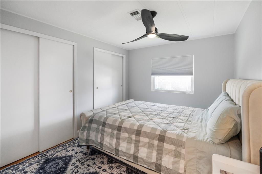 Bedroom featuring two sliding door closets, a single window with blinds, a ceiling fan with integrated lighting, and wood-finish flooring