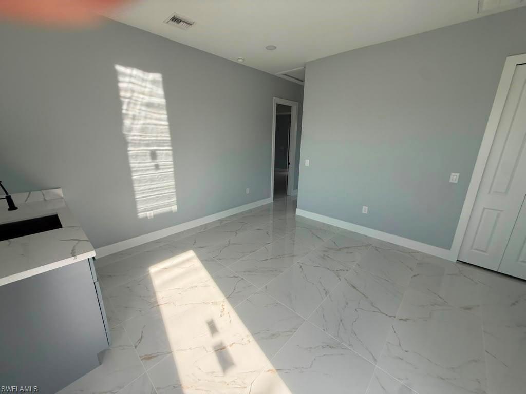 Open-concept living space featuring a textured accent wall with an integrated electric fireplace, a modern kitchen island with pendant lighting, white shaker-style cabinetry, and large format porcelain tile flooring throughout
