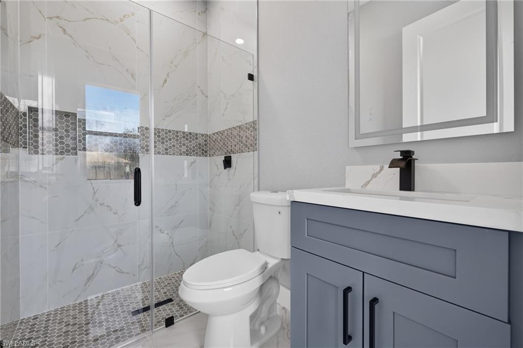 Walk-in shower with clear glass enclosure, white marble-look tile, and a mosaic accent band