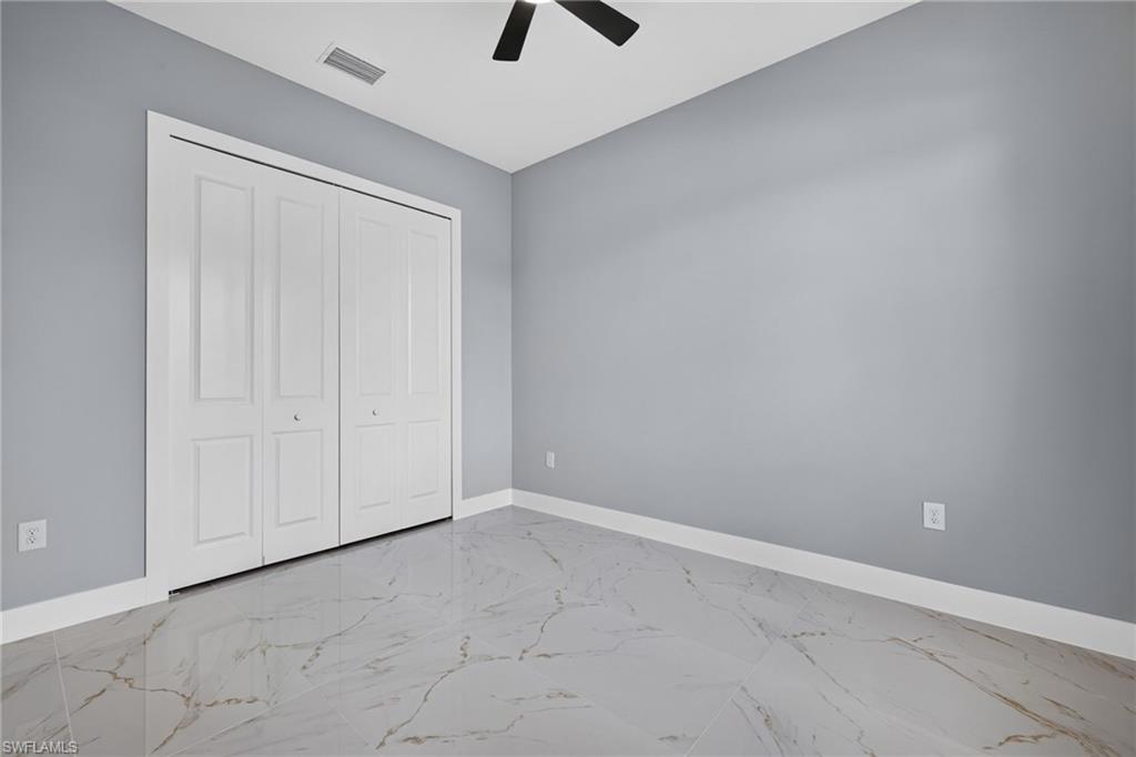 Spacious room featuring light gray walls, marble-look tile flooring, and a ceiling fan