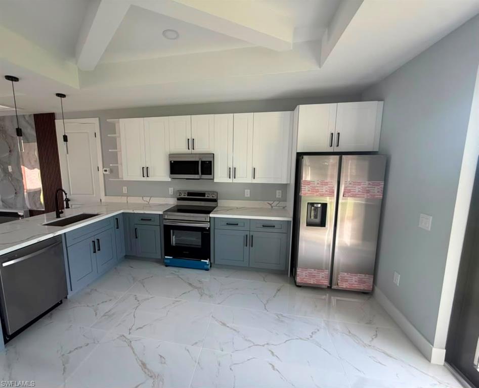Modern kitchen featuring white and blue two-tone cabinetry, stainless steel appliances, and a central island with pendant lighting