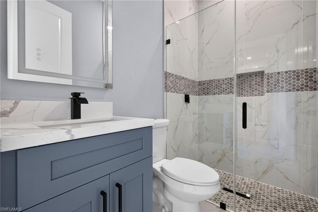 Modern bathroom featuring a glass-enclosed shower with honeycomb tile accent, white marble-look shower walls, a dark blue vanity with quartz-look countertop, and a sleek black faucet