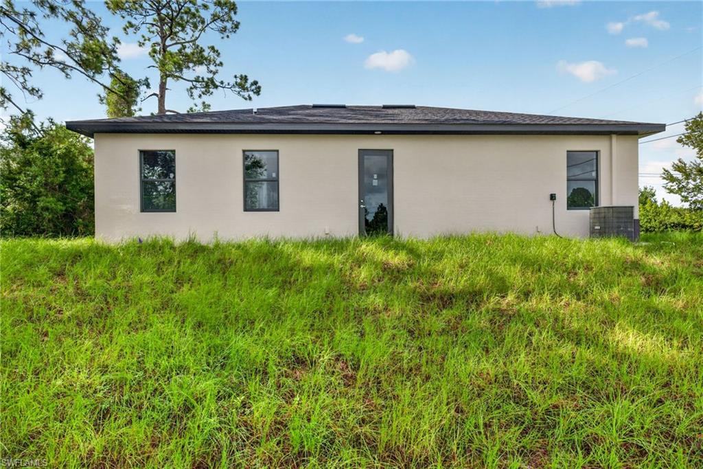 Rear exterior featuring a stucco finish, dark framed windows, a dark framed door, and a visible HVAC unit