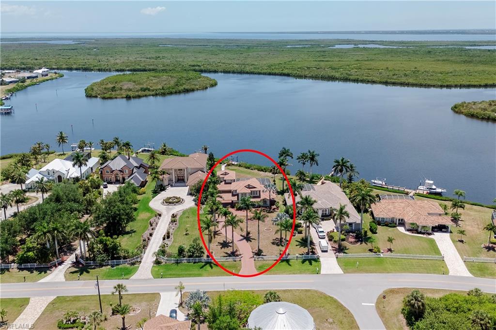 Waterfront property featuring a tile roof, mature palm trees, a circular brick paver driveway, an attached garage, and a waterfront dock