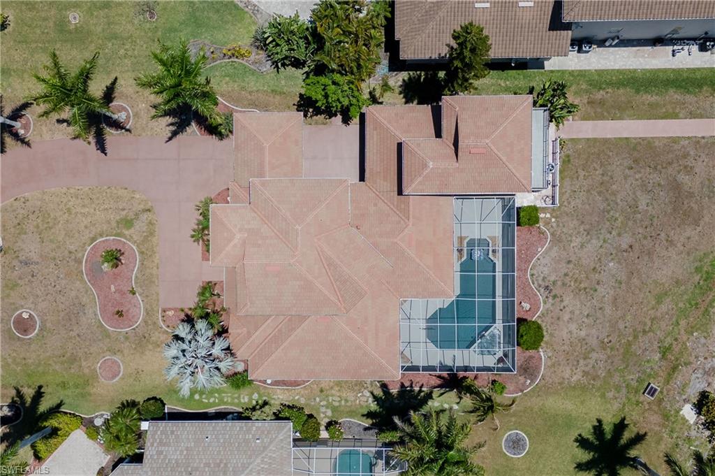 Spacious property featuring a large residence with a multi-level tile roof, an expansive screened-in swimming pool, a concrete driveway, and mature landscaping