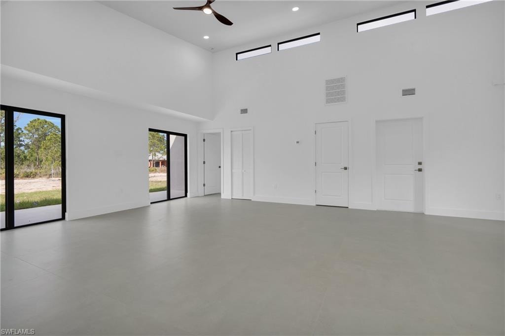 Empty room featuring ceiling fan, concrete flooring, recessed lighting, and a towering ceiling
