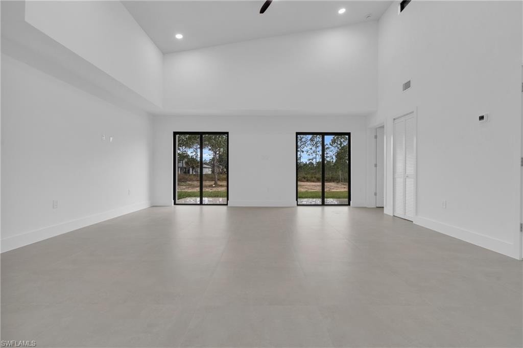 Empty room with a towering ceiling, ceiling fan, concrete floors, and recessed lighting