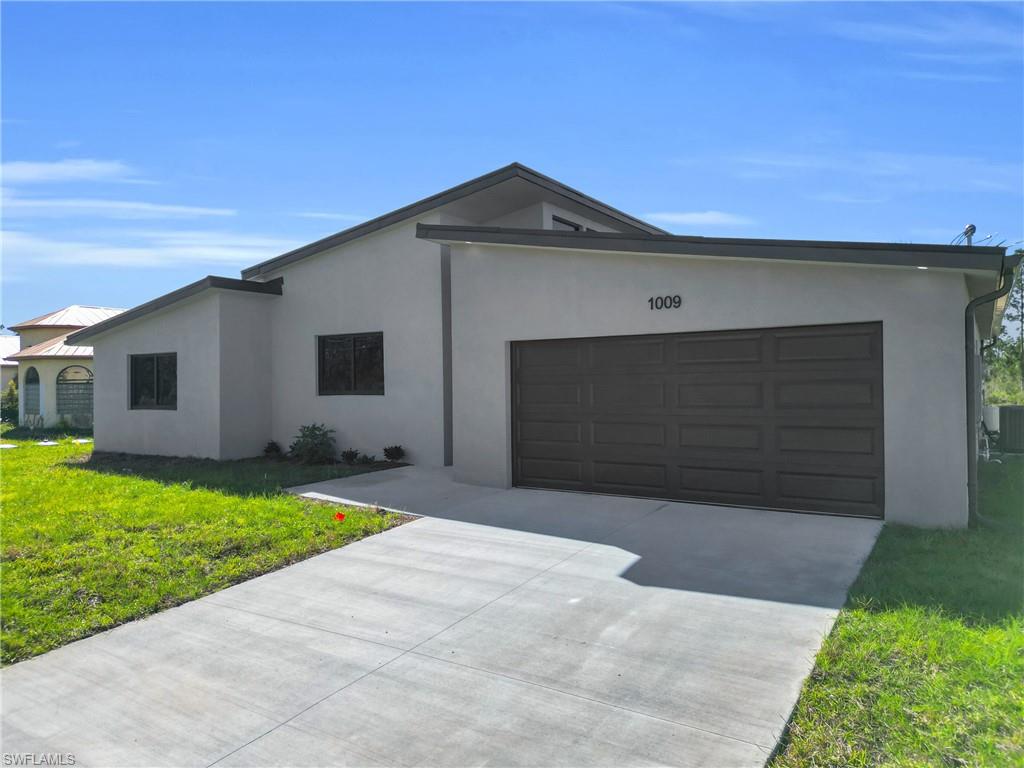Ranch-style home with a front yard, stucco siding, driveway, and an attached garage