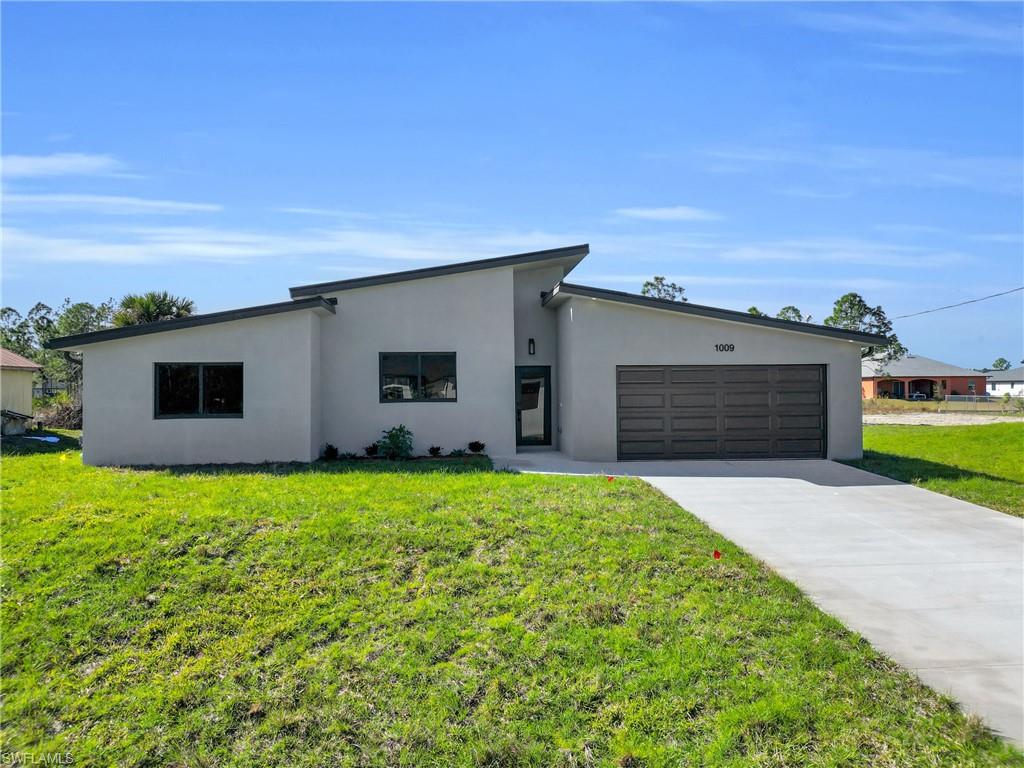 Mid-century modern home featuring a front lawn, stucco siding, concrete driveway, and a garage