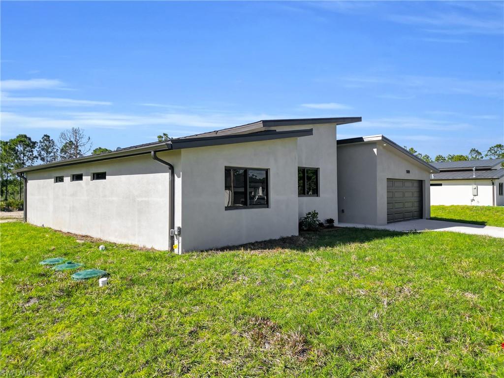 View of property exterior with a lawn, stucco siding, a garage, and driveway