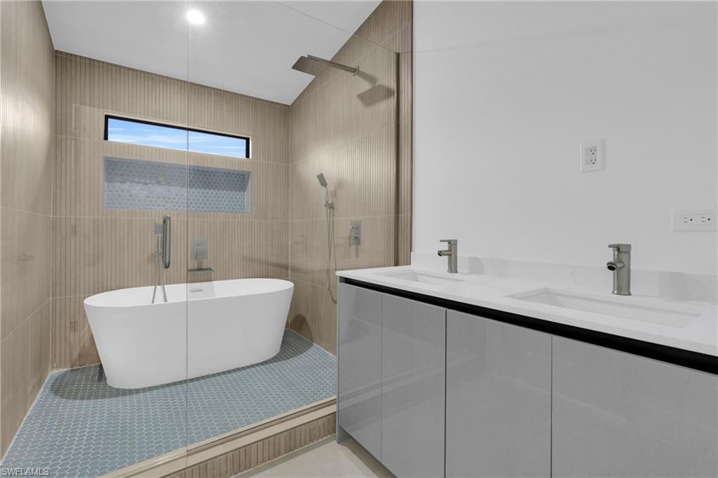 Full master bathroom with double vanity, a walk in shower, a soaking tub, tile patterned flooring, and tile walls