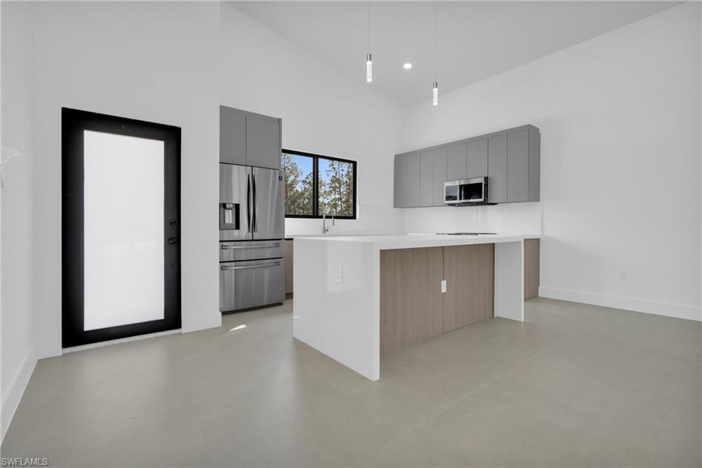 Kitchen featuring gray cabinetry, high vaulted ceiling, a kitchen island, stainless steel appliances, and modern cabinets