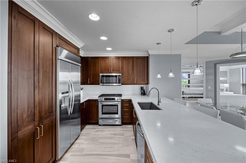 Kitchen featuring hanging light fixtures, light stone counters, stainless steel appliances, sink, and kitchen peninsula