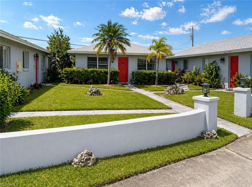 Manicured green lawn with concrete walkways, framed by a low white stucco wall and substantial stucco pillars featuring exterior light fixtures