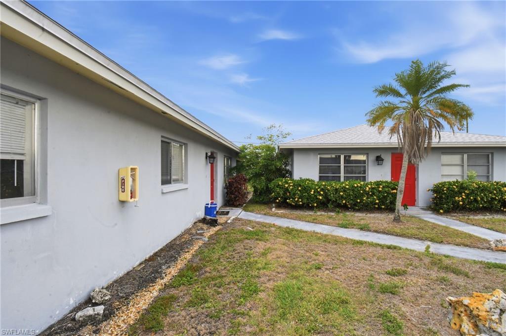 Single-story residence featuring light gray exterior siding, a red entry door, white trim, and a mature palm tree