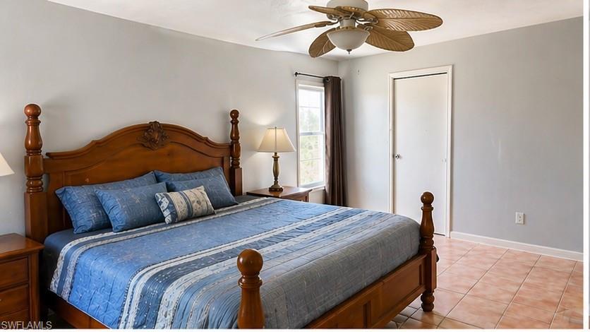 Spacious room featuring light gray walls, a window with brown drapes, a ceiling fan with palm-leaf style blades, and light-toned tile flooring