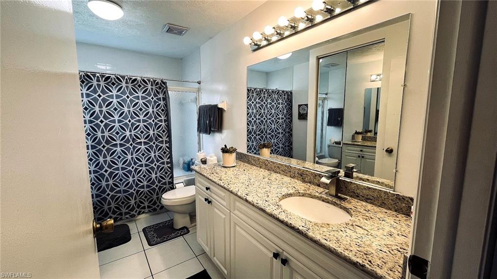 Bathroom vanity featuring a granite countertop with an undermount sink, white cabinetry with dark hardware, and an expansive mirror