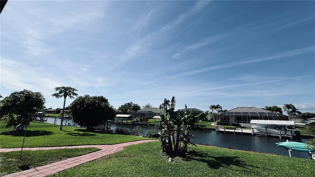 Waterfront property featuring a private boat dock with lift, canal access, a brick-laid pathway, mature landscaping, and a manicured lawn