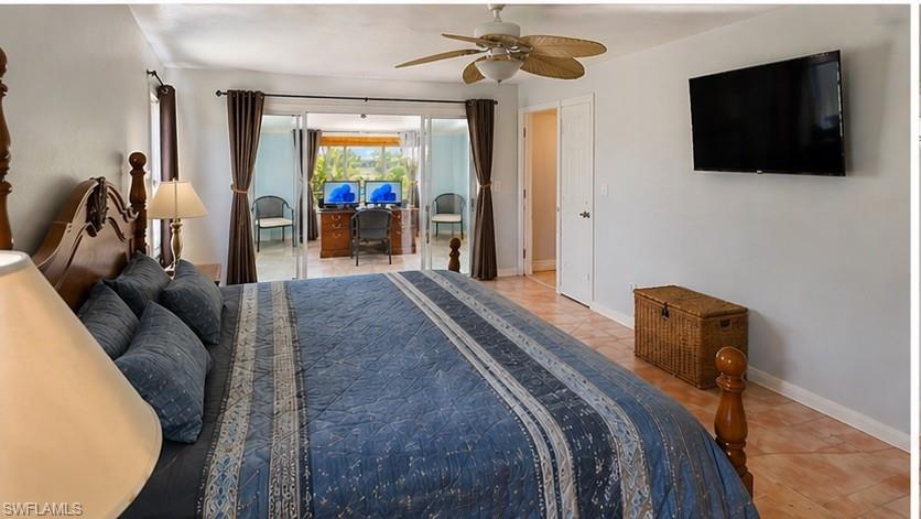 Bedroom featuring terracotta-style floor tiles, a ceiling fan, and sliding glass doors opening to an adjacent space with an exterior view