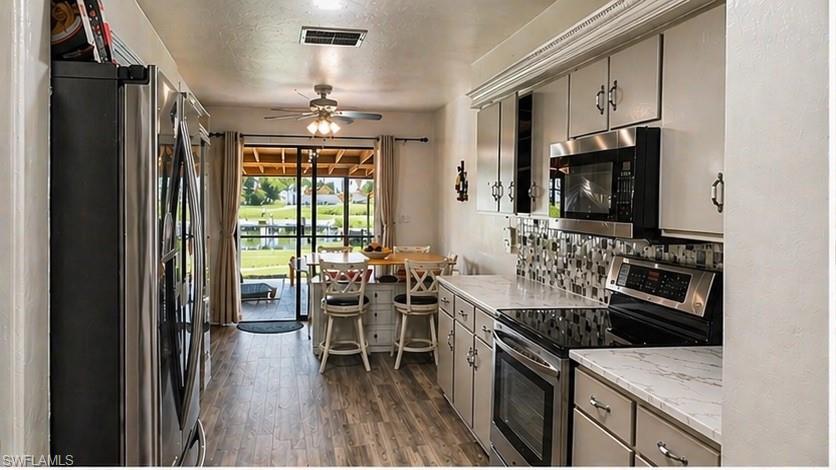 Kitchen featuring light cabinetry, stainless steel appliances, patterned tile backsplash, wood-finish flooring, and a breakfast bar with seating