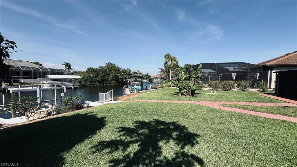 Waterfront property featuring a private boat dock, lush green lawn, mature tropical landscaping, and a screened outdoor enclosure