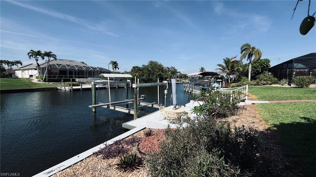 Waterfront property featuring a private boat dock with lift, concrete seawall, established landscaping, screened lanai, and mature palm trees