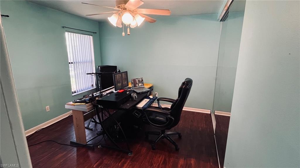 Room featuring wood-finish flooring, a ceiling fan with light fixture, and a window with vertical blinds
