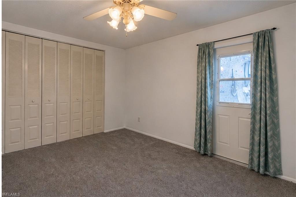 Carpeted room featuring a white ceiling and walls, a ceiling fan with light fixture, a door with a window, and accordion-style closet doors