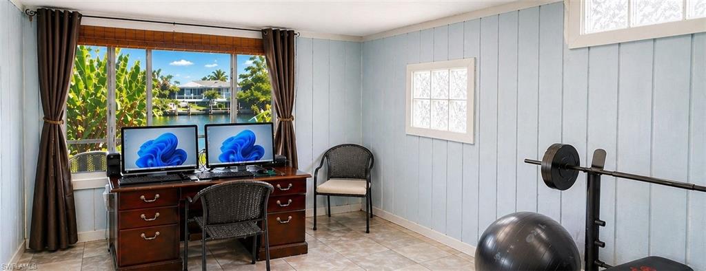 Spacious room featuring light blue vertical paneling, tiled flooring, and multiple windows