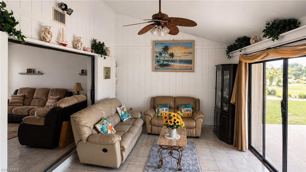 Living area featuring vaulted ceilings with a ceiling fan, white paneled walls, and tile flooring