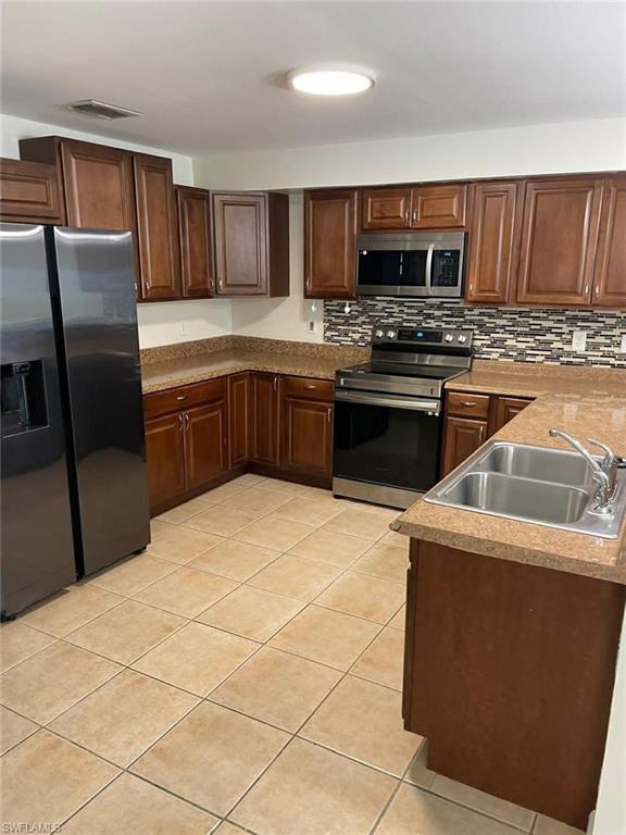 Updated kitchen with rich wood-tone cabinetry, stainless steel appliances, decorative tile backsplash, and tile flooring — move-in ready