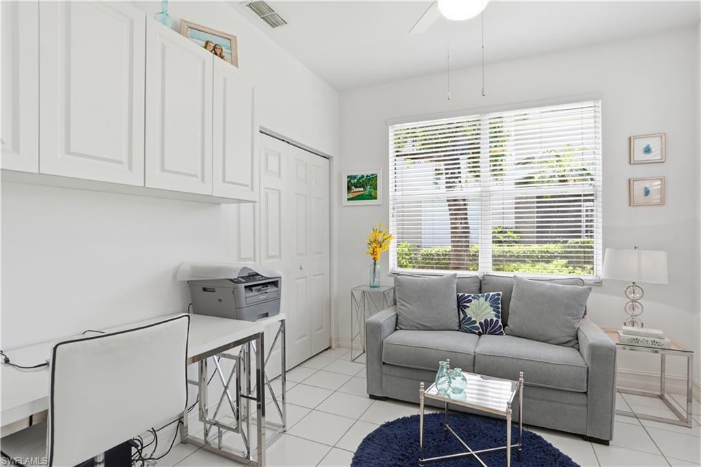Bright room featuring tile flooring, a large window with blinds, a ceiling fan, and white cabinetry