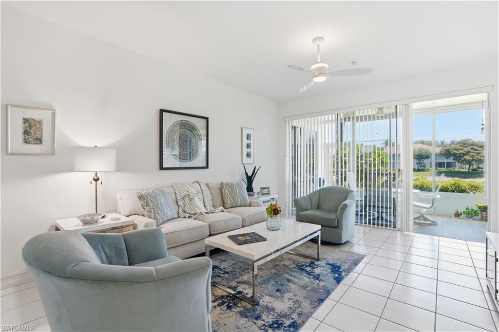 Bright living space with white tile flooring and a patio featuring a white railing, accessible via a large glass sliding door with vertical blinds