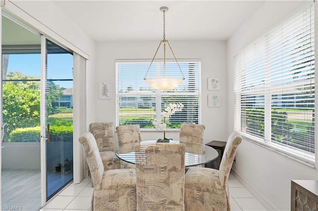 Dining area featuring white ceramic tile flooring, a glass-top table, multiple windows with blinds, a sliding glass door to a screened patio, and a central pendant light fixture