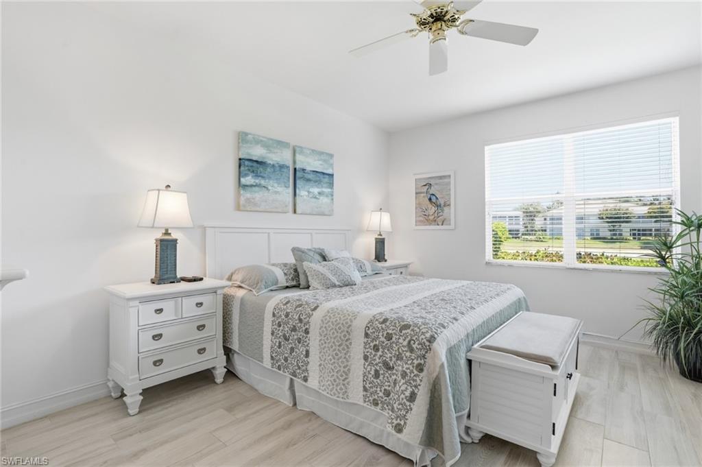 Bright bedroom featuring light wood-finish flooring, a ceiling fan, and a large window with horizontal blinds