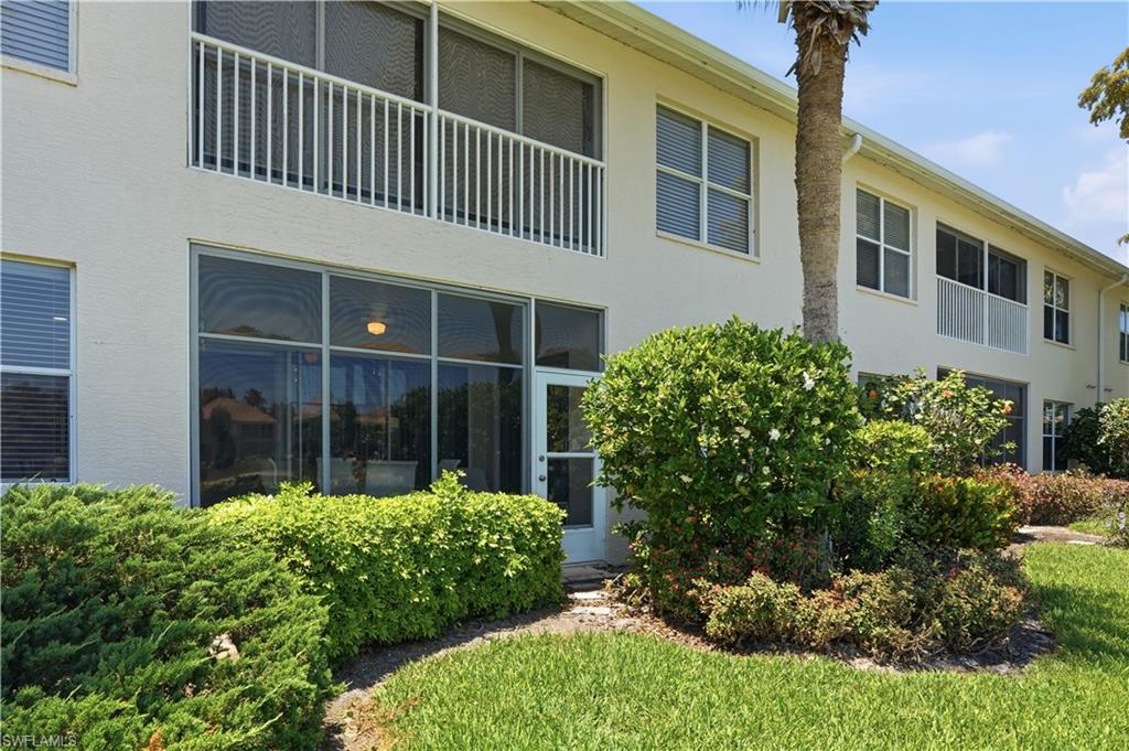 Exterior featuring a screened-in patio, white aluminum balcony railing, stucco siding, multiple windows with blinds, and mature landscaping